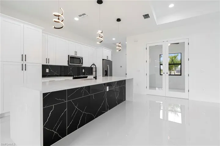 Kitchen featuring appliances with stainless steel finishes, sink, decorative light fixtures, a center island with sink, and white cabinetry