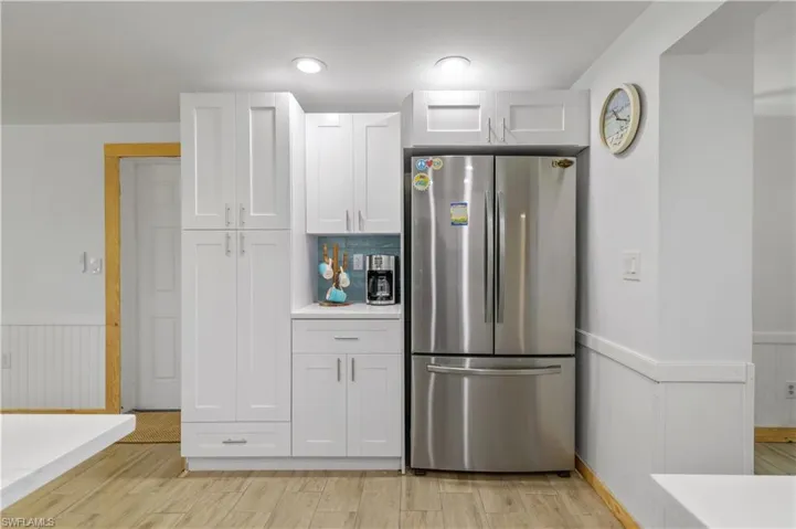 Kitchen featuring a wainscoted wall, freestanding refrigerator, light countertops, white cabinets, and light wood-style floors