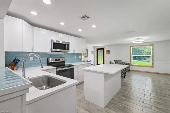 Kitchen featuring a wainscoted wall, a sink, a center island, white cabinetry, and appliances with stainless steel finishes