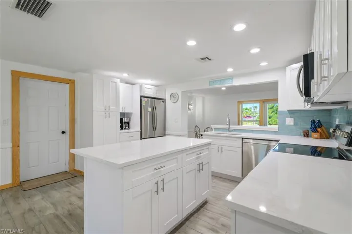 Kitchen with light wood-type flooring, visible vents, a kitchen island, backsplash, and appliances with stainless steel finishes