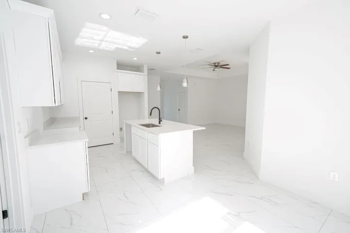 Kitchen featuring decorative light fixtures, white cabinets, a center island with sink, light marble finish flooring, and recessed lighting.Photos are of a staged model or similar plan. Features and finishes may vary.