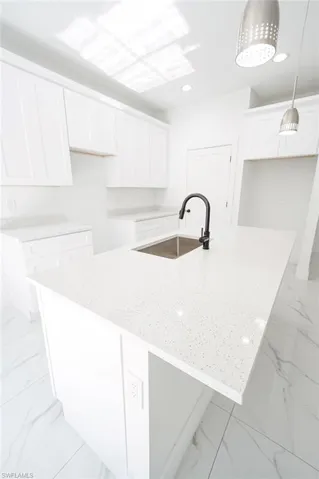 Kitchen featuring white cabinets, light stone countertops, an island with sink, hanging light fixtures, and light marble finish floors. Photos are of a staged model or similar plan. Features and finishes may vary.