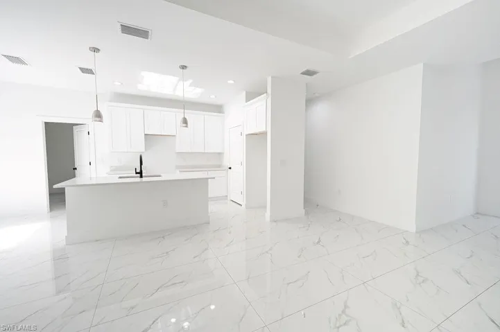 Kitchen with white cabinets, a center island with sink, hanging light fixtures, open floor plan, and light marble finish floors. Photos are of a staged model or similar plan. Features and finishes may vary.