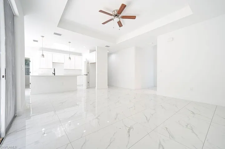 Unfurnished living room featuring a tray ceiling, ceiling fan, and light marble finish flooring. Photos are of a staged model or similar plan. Features and finishes may vary.