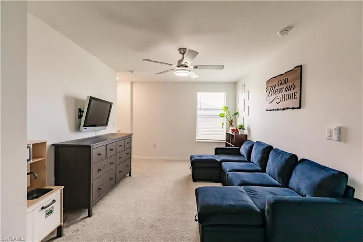 Carpeted living room featuring ceiling fan and sink