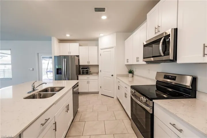 Kitchen with white cabinets, light tile patterned floors, appliances with stainless steel finishes, light stone counters, and sink