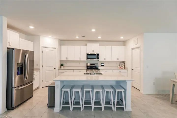 Kitchen featuring a kitchen island with sink, appliances with stainless steel finishes, white cabinetry, and a breakfast bar area
