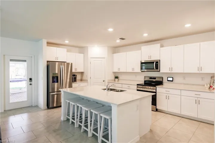 Kitchen featuring a breakfast bar area, appliances with stainless steel finishes, a kitchen island with sink, sink, and white cabinets