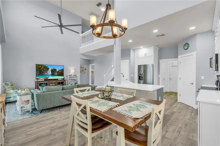 Dining area with stairs, ceiling fan with notable chandelier, a towering ceiling, light wood finished floors, and visible vents