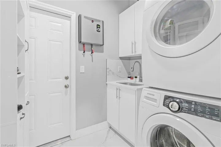 Laundry area with light marble finish flooring, stacked washer / dryer, and cabinet space