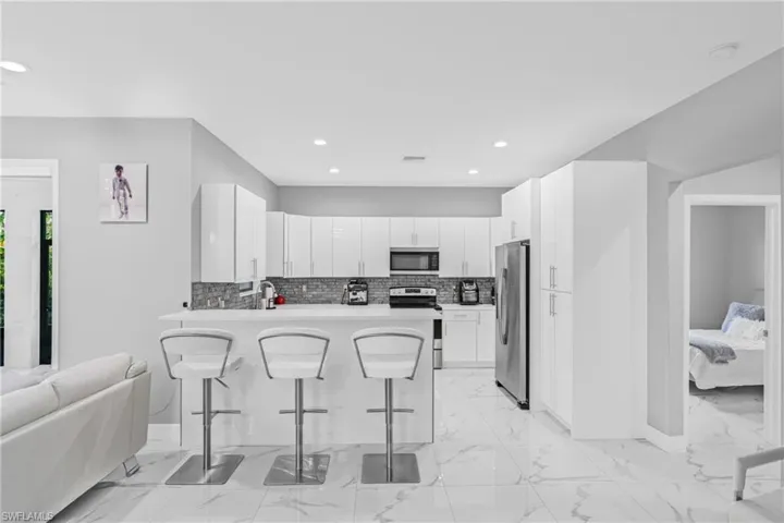 Kitchen featuring a breakfast bar, light marble finish floors, decorative backsplash, white cabinetry, and appliances with stainless steel finishes
