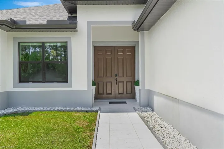 Doorway to property featuring stucco siding, a shingled roof, and a yard