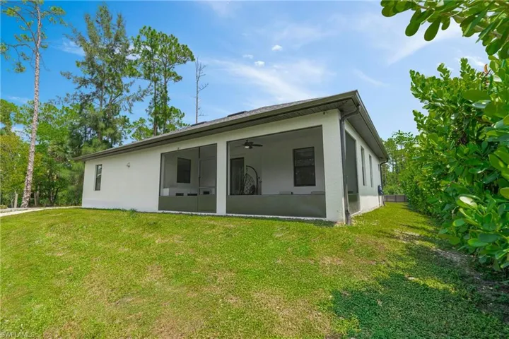 Rear view of property featuring stucco siding, a yard, and a ceiling fan