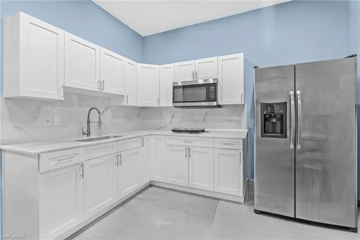 Kitchen featuring tasteful backsplash, stainless steel appliances, white cabinetry, and light stone counters