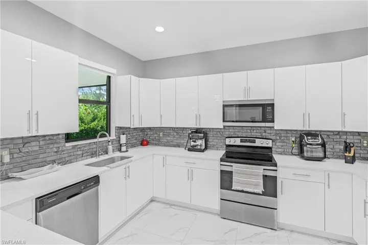 Kitchen with light marble finish floors, appliances with stainless steel finishes, tasteful backsplash, light stone counters, and recessed lighting