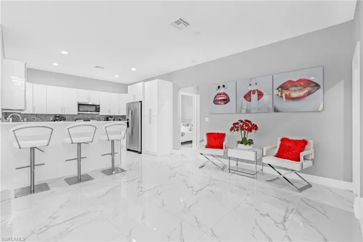 Kitchen featuring white cabinets, a kitchen bar, light marble finish flooring, appliances with stainless steel finishes, and a peninsula