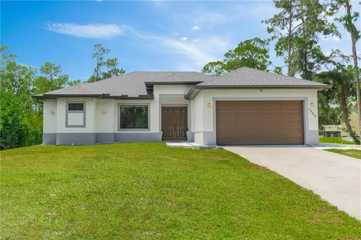 Prairie-style home featuring an attached garage, stucco siding, a front lawn, and driveway