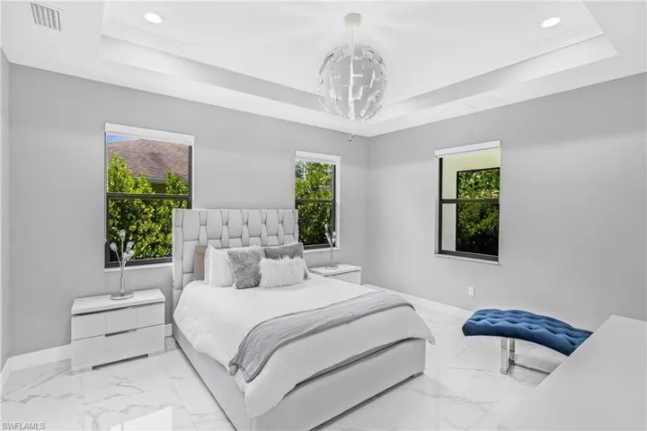 Bedroom featuring a raised ceiling, marble finish floors, and recessed lighting