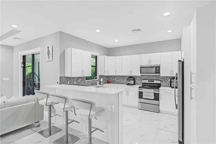Kitchen featuring light marble finish flooring, appliances with stainless steel finishes, a kitchen breakfast bar, decorative backsplash, and recessed lighting