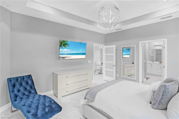 Bedroom featuring light marble finish floors, a raised ceiling, ensuite bathroom, and a chandelier