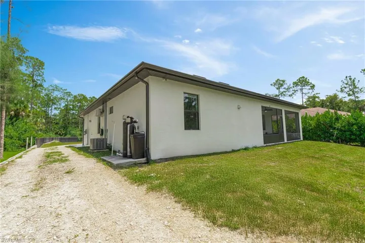 Rear view of property with stucco siding, dirt driveway, and a lawn
