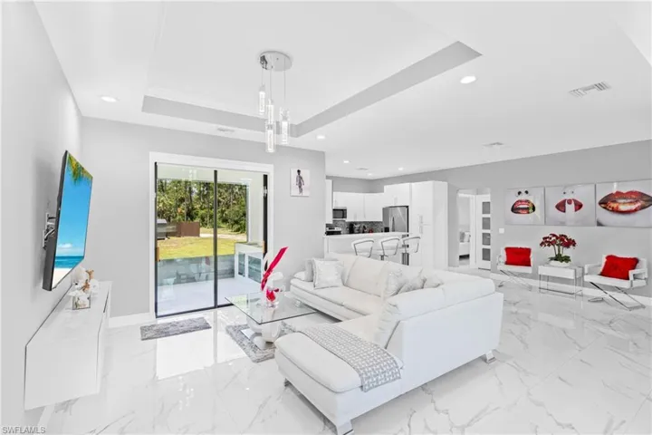 Living area featuring a tray ceiling, recessed lighting, and light marble finish flooring