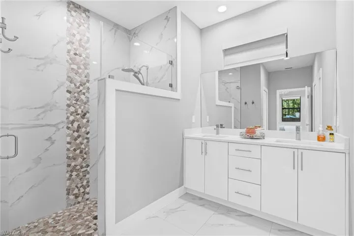 Full bath with light marble finish flooring, a marble finish shower, and double vanity