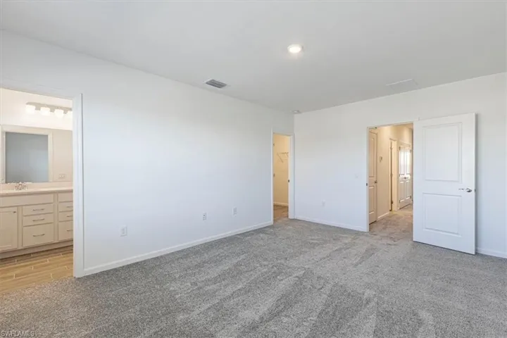Unfurnished bedroom with a walk in closet, light carpet, and ensuite bath