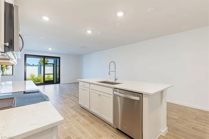 Kitchen with appliances with stainless steel finishes, an island with sink, wood tiled floors, light stone counters, and recessed lighting