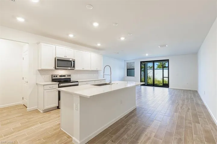 Kitchen featuring stainless steel appliances, white cabinetry, a center island with sink, wood finish floors, and recessed lighting