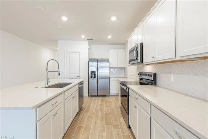 Kitchen featuring stainless steel appliances, light stone counters, white cabinetry, a center island with sink, and tasteful backsplash