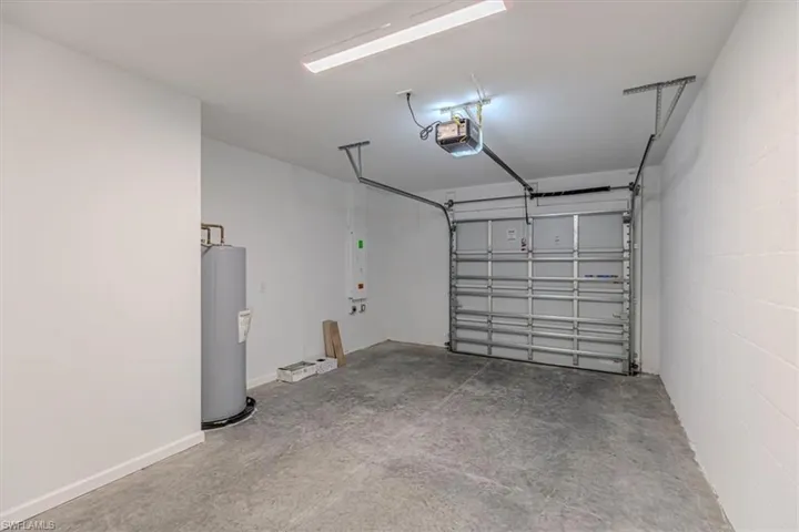 Garage featuring water heater, concrete block wall, and a garage door opener
