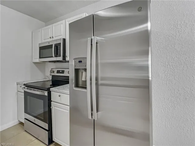 Kitchen featuring appliances with stainless steel finishes, white cabinets, light countertops, light tile patterned flooring, and a textured wall