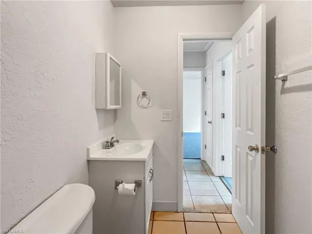 Half bathroom featuring tile patterned floors, a textured wall, and vanity