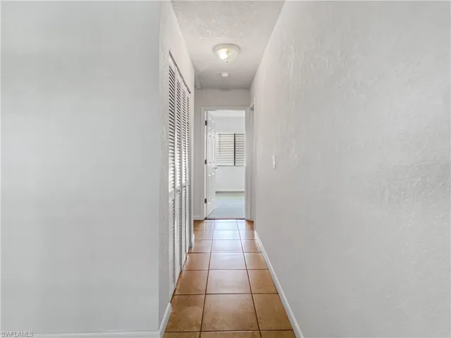 Hallway with a textured ceiling, a textured wall, and light tile patterned floors