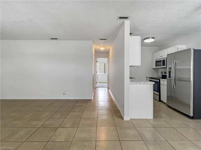 Kitchen with appliances with stainless steel finishes, light countertops, a textured ceiling, white cabinets, and light tile patterned flooring