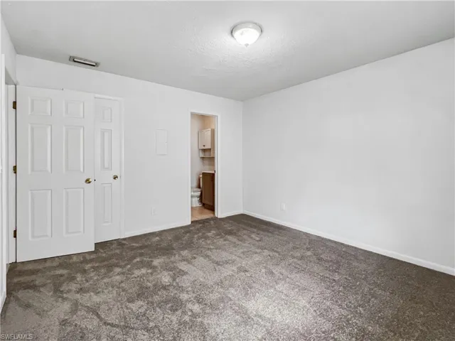 Unfurnished bedroom featuring carpet floors, a textured ceiling, and ensuite bath