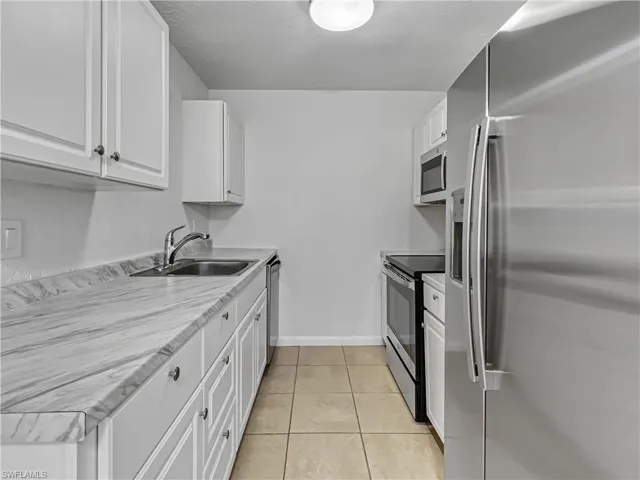Kitchen with appliances with stainless steel finishes, white cabinetry, light tile patterned flooring, light countertops, and a textured ceiling