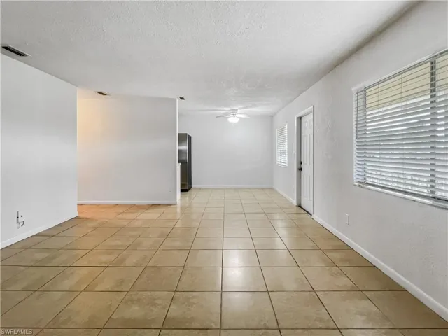 Empty room with a ceiling fan, a textured ceiling, light tile patterned flooring, and a textured wall