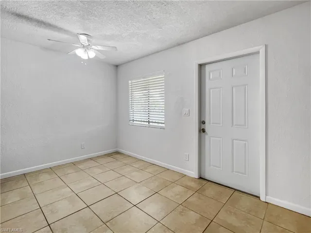 Unfurnished room with a textured wall, a textured ceiling, a ceiling fan, and light tile patterned flooring