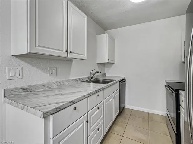 Kitchen with appliances with stainless steel finishes, white cabinetry, light countertops, light tile patterned floors, and a textured ceiling