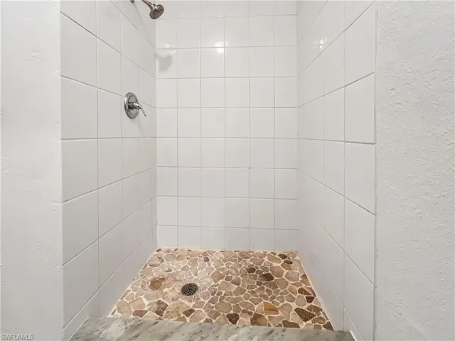 Full bathroom featuring a textured wall and tiled shower