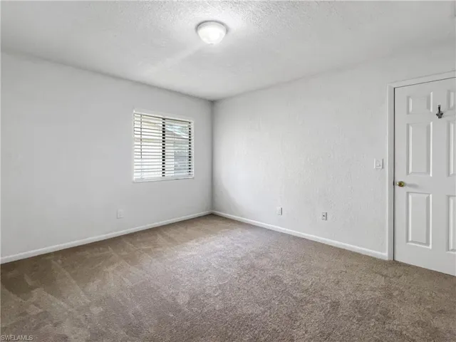 Carpeted empty room featuring a textured ceiling and a textured wall