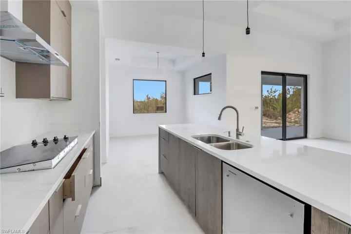 Kitchen with a tray ceiling, wall chimney exhaust hood, light stone counters, and hanging light fixtures