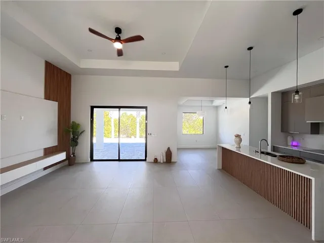 Kitchen with ceiling fan, modern cabinets, light stone counters, pendant lighting, and open floor plan