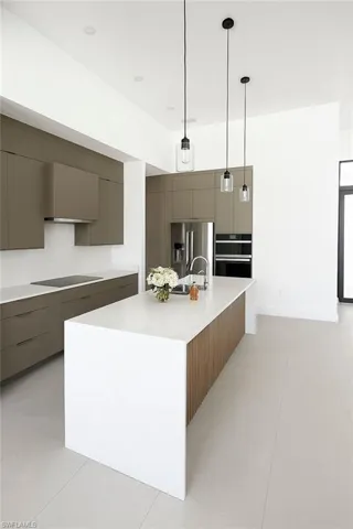 Kitchen featuring modern cabinets, gray cabinetry, a kitchen island with sink, and decorative light fixtures