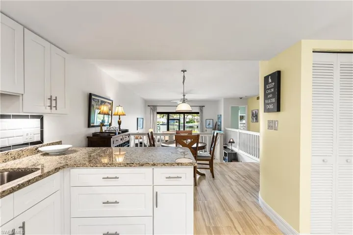 Kitchen with light hardwood / wood-style flooring, kitchen peninsula, light stone counters, hanging light fixtures, and white cabinets