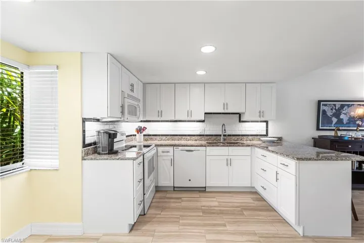 Kitchen with backsplash, sink, white appliances, and white cabinets