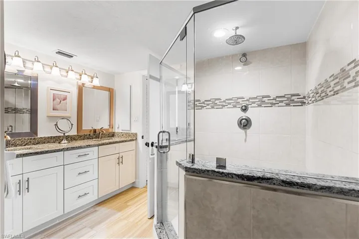 Bathroom with dual bowl vanity, an enclosed shower, and hardwood / wood-style flooring