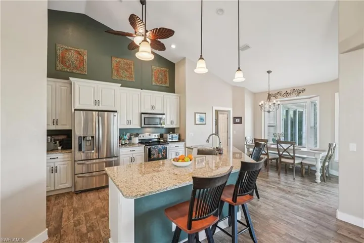 Kitchen with stainless steel appliances, a kitchen bar, hanging light fixtures, ceiling fan, and light stone countertops